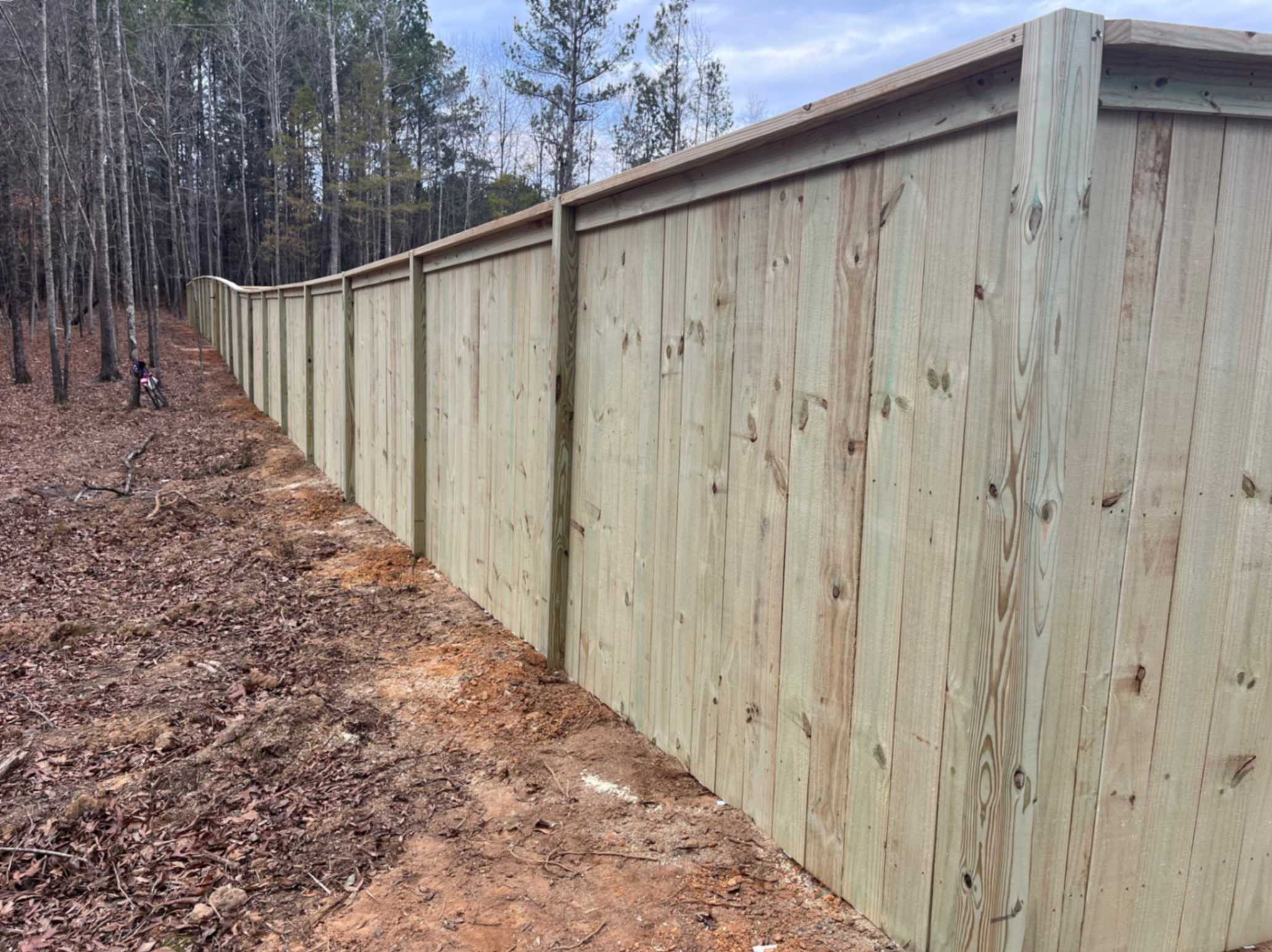 Professional Wood Fencing in Athens, GA, Fence installer measuring gate opening beside a sloped residential yard