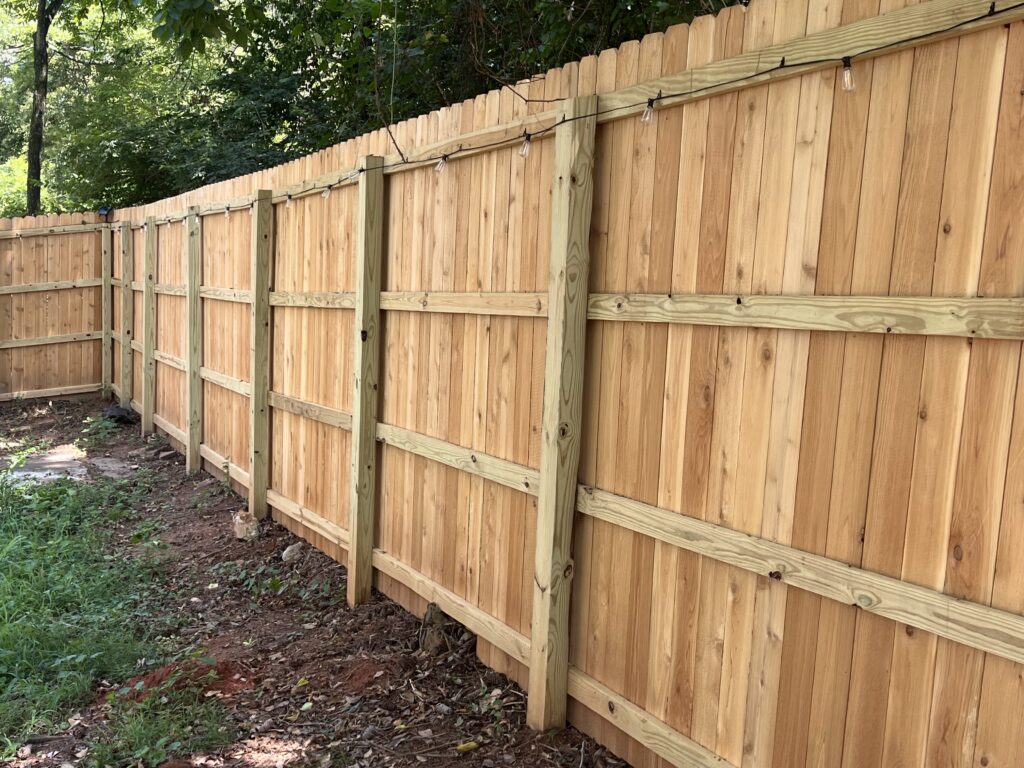 Installer measuring fence line carefully along residential property boundary with professional tools
